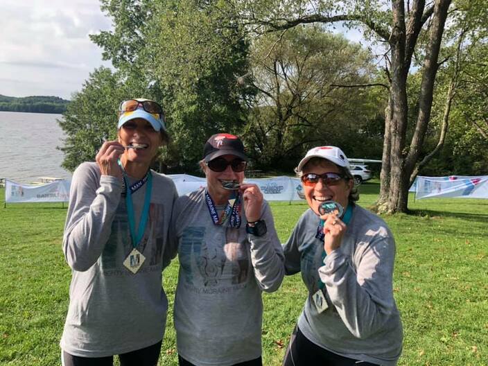 3 women biting finishers medal in MMM shirts