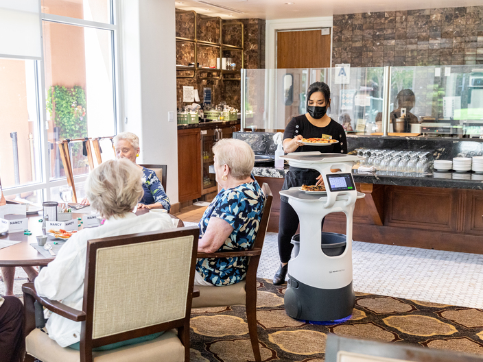 Bear Robotics' autonomous robot server assists a staff member in serving food to residents of La Costa Glen senior living center. 
